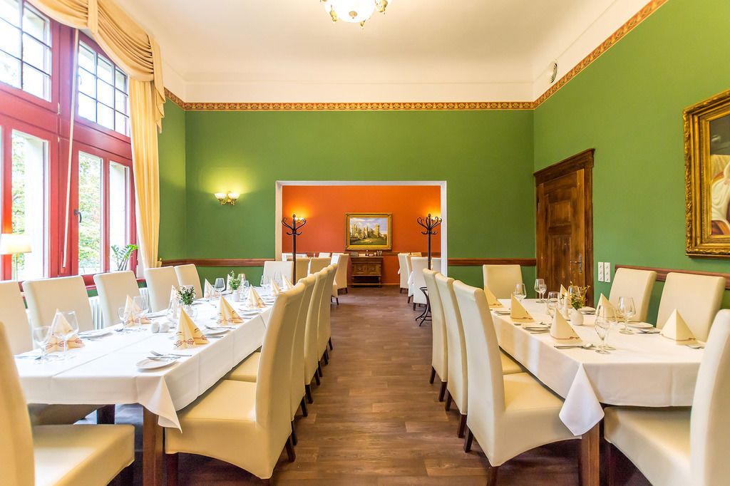 Een eethoek met gedekte tafels, een uitzicht op de stad door het raam en een groene wand met een schilderij.