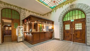 A lobby with a reception desk, a refrigerator, and a staircase leading to an upper floor. - Waldschlösschen Wangen (Nebra)