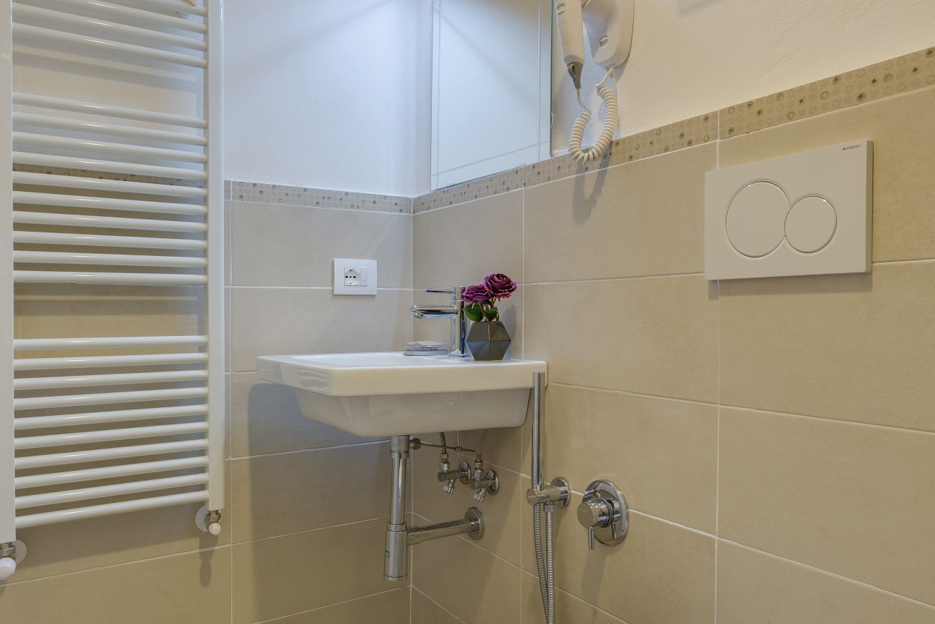 Ein Badezimmer mit einem weißen Waschbecken, einer Dusche, einem Handtuchhalter und einer Wandheizung.
