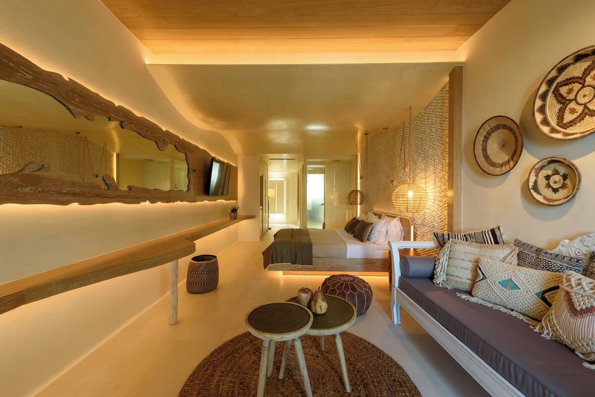A modern living room with a sofa, a coffee table, and a small side table. There is a large mirror on the wall and a hanging light fixture.