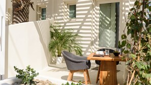 A wooden table with a chair, a potted plant, and a small table with a glass and a bowl. - Divelia East (Santorini)