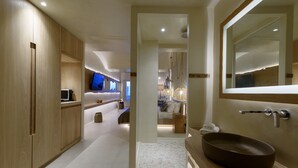 A modern bathroom with a large mirror, wooden cabinets, and a round sink. - Divelia East (Santorini)