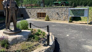Una estatua de una figura vestida con atuendo tradicional, un muro de piedra, un tractor verde y un letrero.