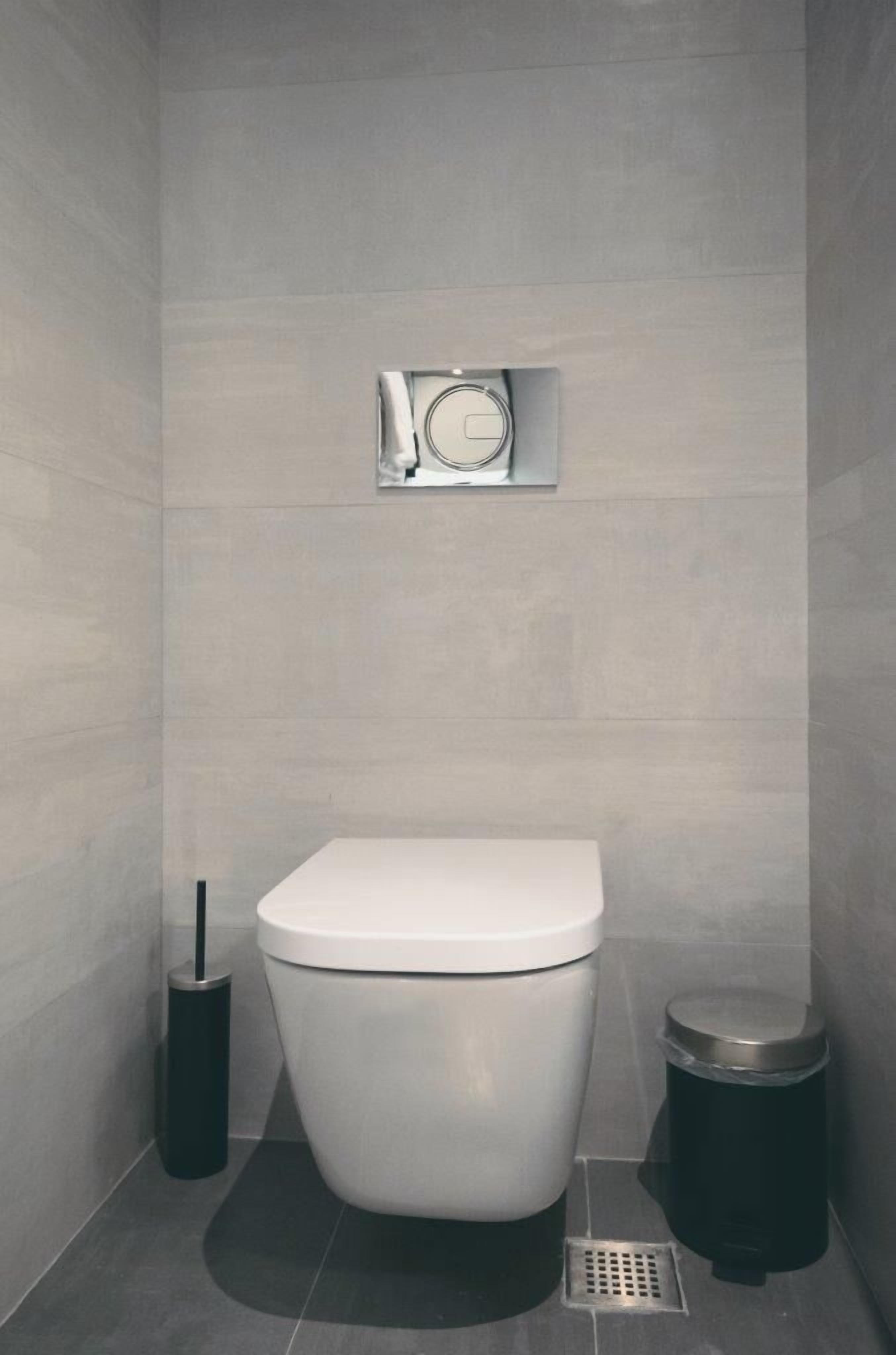 Uma casa de banho moderna com sanita, um contentor de lixo e uma prateleira fixada na parede.