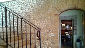 Un escalier en pierre, agrémenté d’une rampe en fer forgé, mène à une pièce dont le mur est en pierre et la porte en bois.