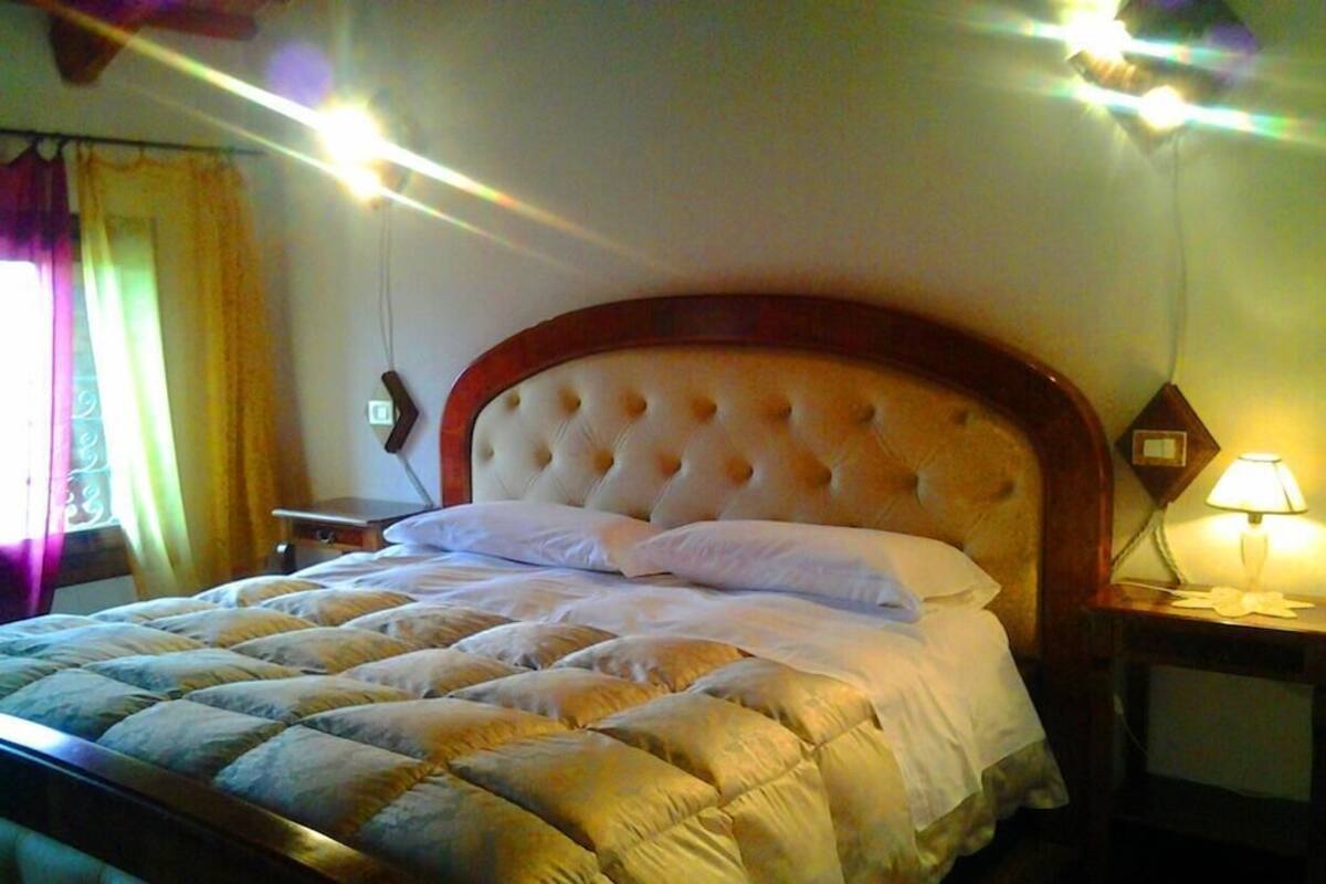 Una cama bien tendida con un cabecero capitonado, una lámpara de noche y una mesita de noche.