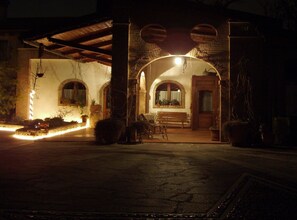 A warmly lit outdoor patio area with a bench, potted plants, and a wooden door. - Agriturismo Melo in Fiore (Maser)