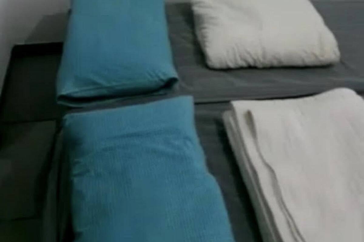 Ein kleines, schlichtes Zimmer mit zwei Betten, jeweils mit Kissen und Decke.
