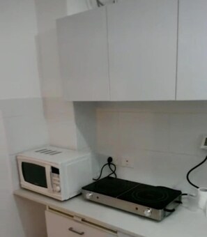 A kitchen with white cabinets, a microwave, a stove, and a roll of paper towels. - Studio Apartments In The Heart Of Haifa (Haifa)