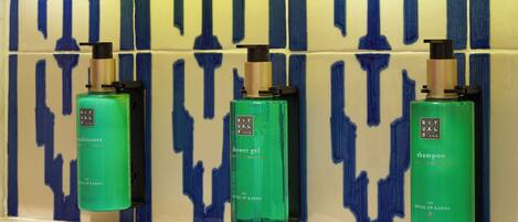 Tres botellas verdes de productos 'Ritual of Karma' sobre una estantería frente a una pared con azulejos azules y beige.