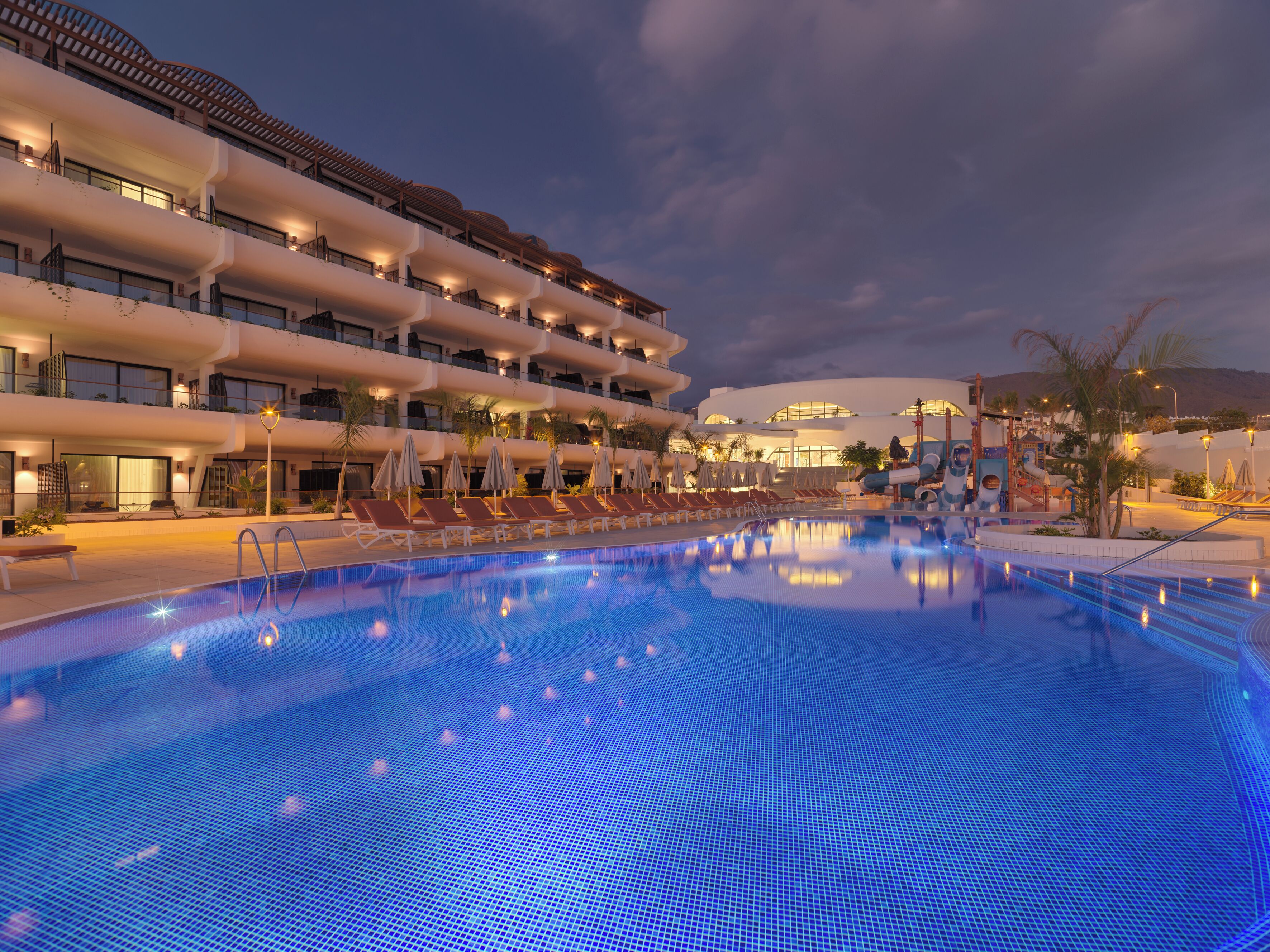 A hotel with a swimming pool, multiple balconies, and a children's play area.