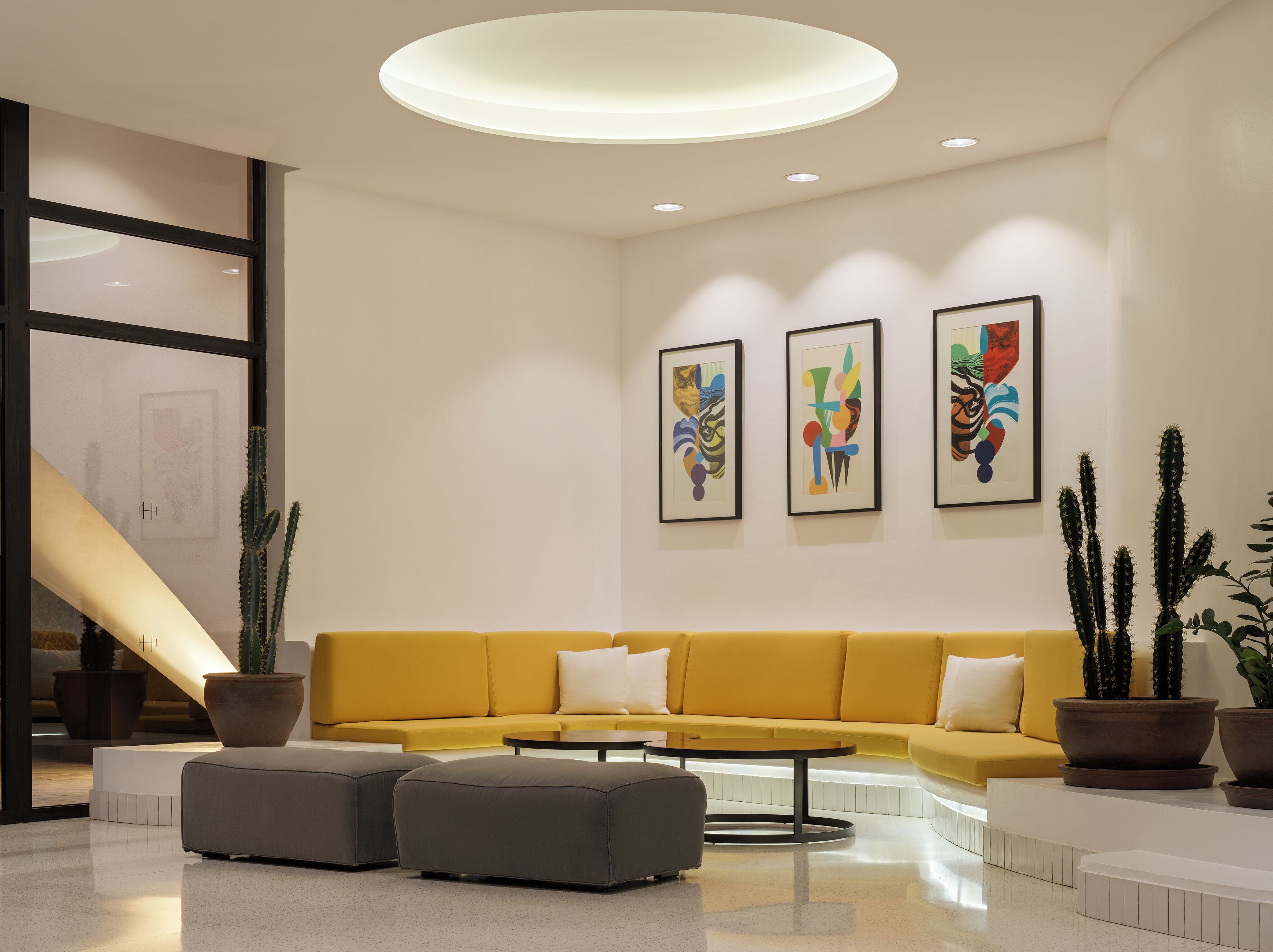 A modern lobby with a yellow sofa, a coffee table, and three framed artworks on the wall.
