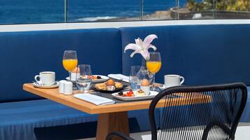 Una mesa de comedor con alimentos para el desayuno y vista al océano.