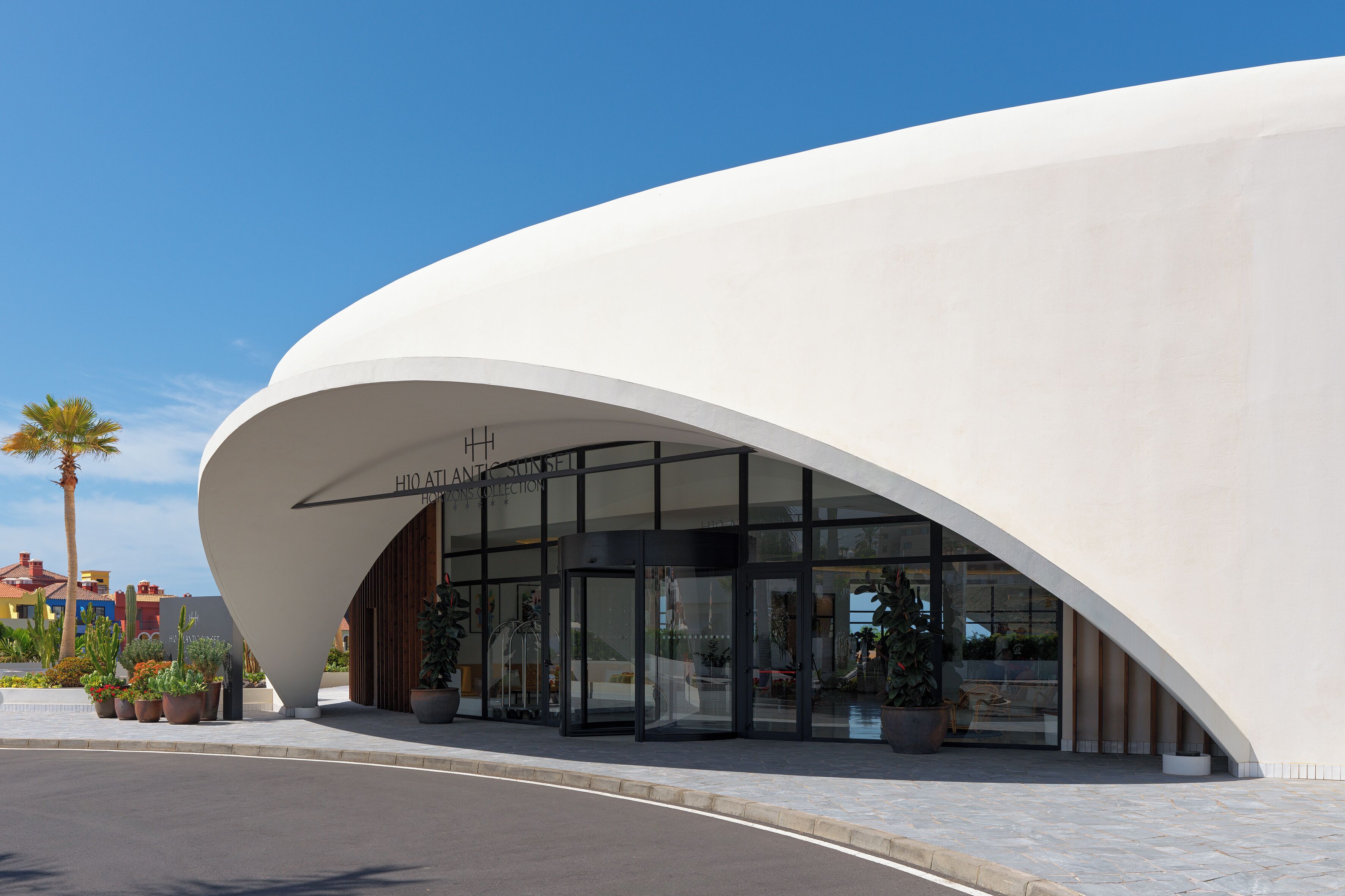 Un bâtiment moderne à la façade blanche et incurvée, doté d’une grande entrée en verre et surplombant un ciel dégagé.