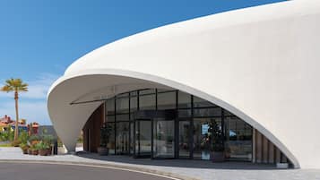 Un bâtiment moderne à la façade blanche et incurvée, doté d’une grande entrée en verre et surplombant un ciel dégagé.