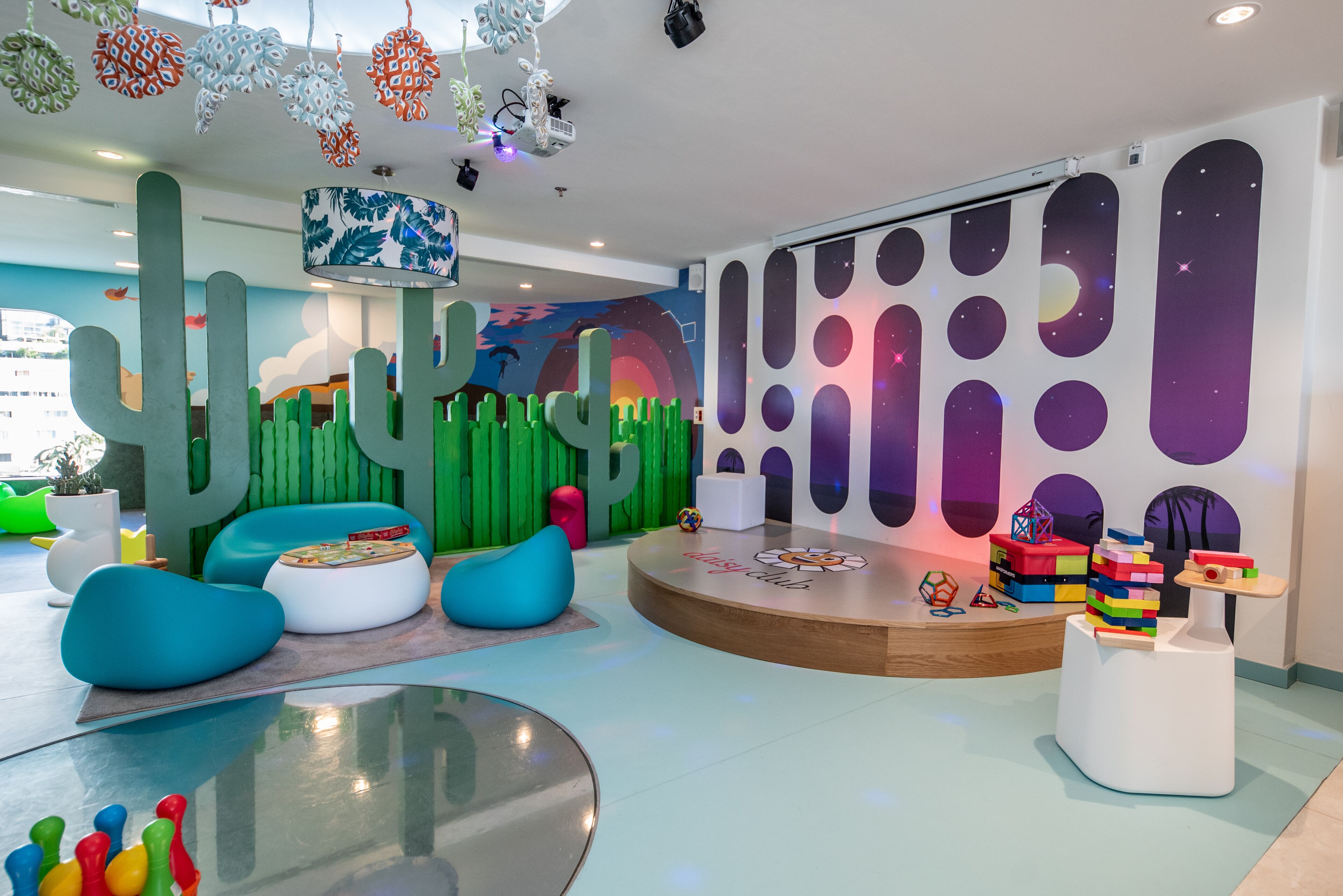 A children's play area with colorful furniture, a cactus-themed wall, and a stage with building blocks.