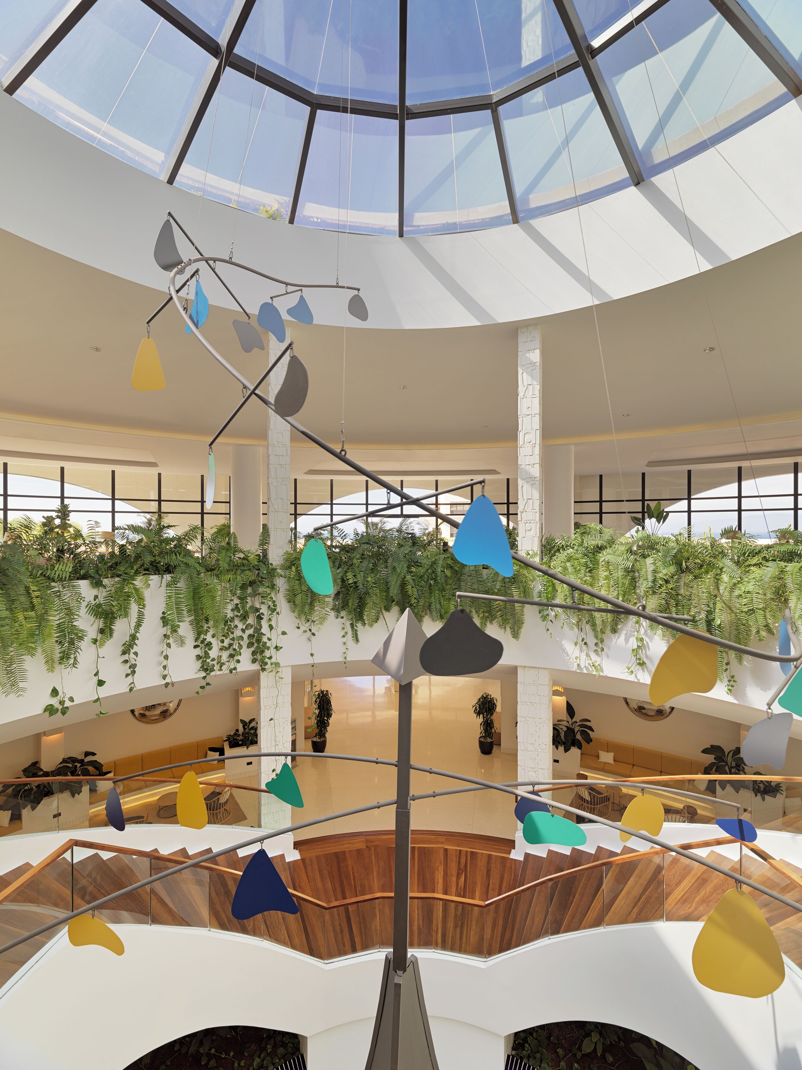 A multi-level atrium with a glass ceiling, wooden flooring, and hanging pendant lights.