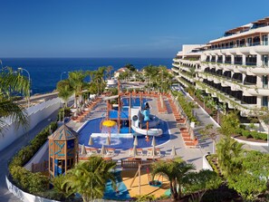 Área de piscina de resort com um toboágua, espreguiçadeiras e vista para o oceano.