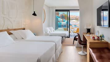 Habitación de hotel con dos camas, un escritorio, una silla, un televisor y vistas a una piscina y edificios.