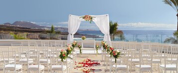 Ceremonia de boda al aire libre con sillas blancas y un arco blanco, con vista al mar.