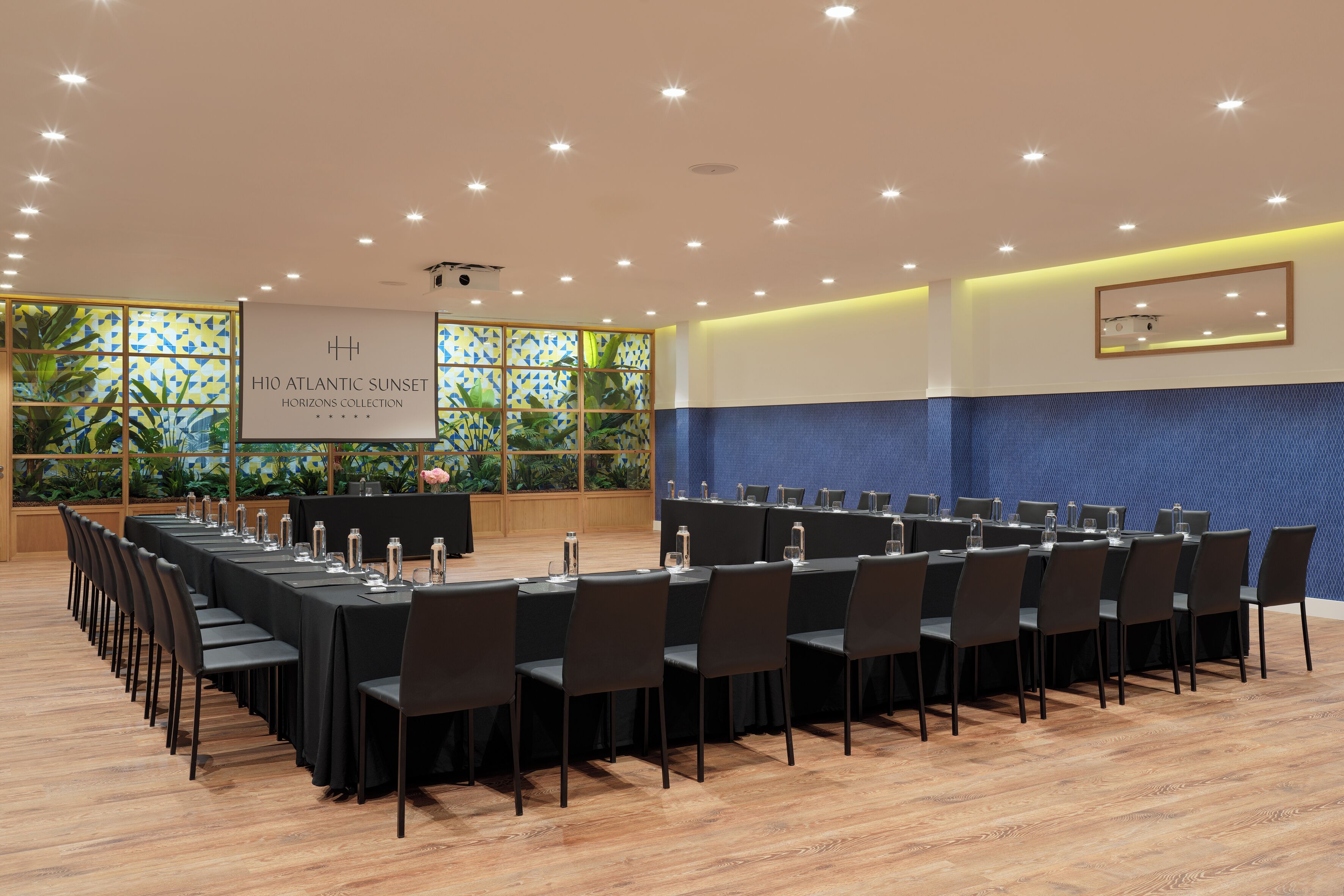 Un salón de conferencias con una larga mesa, sillas y un fondo con un logotipo.