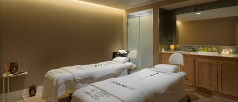 Un cuarto de spa con dos camillas, un armario de madera y un espejo.