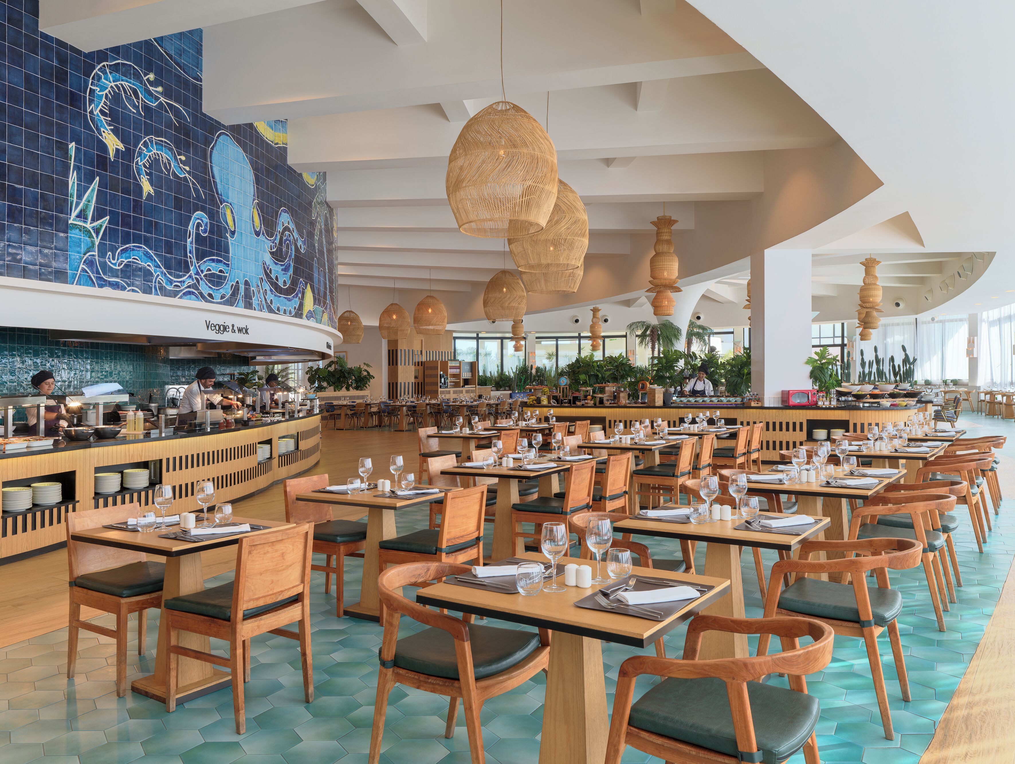 Un restaurante espacioso con barra central, varias mesas para comer y un mural grande en la pared.