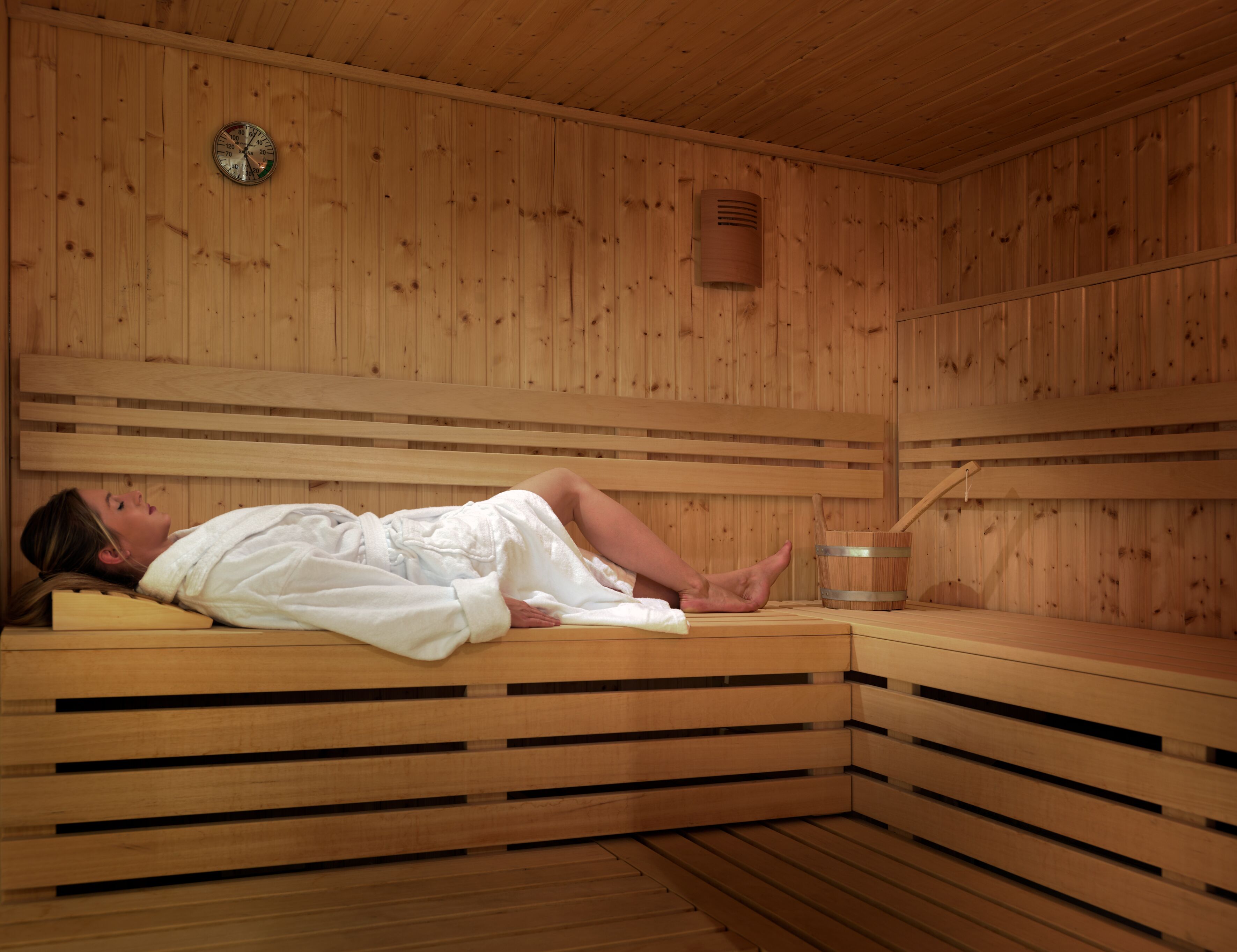A sauna room with wooden walls, a bench, a wooden floor, a towel, and a wooden bucket.