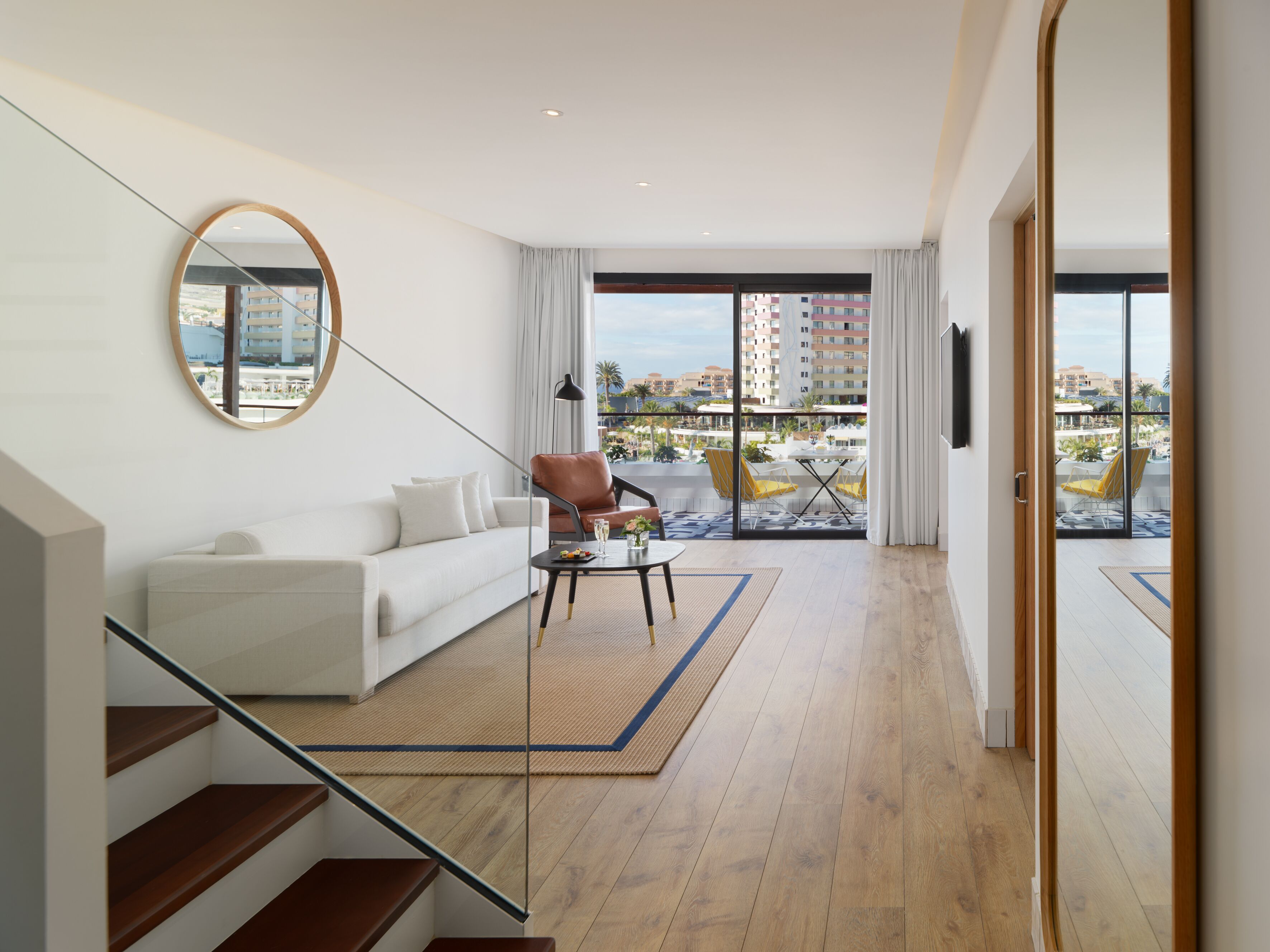 A modern living room with a sofa, a coffee table, and a view of the city through large windows.