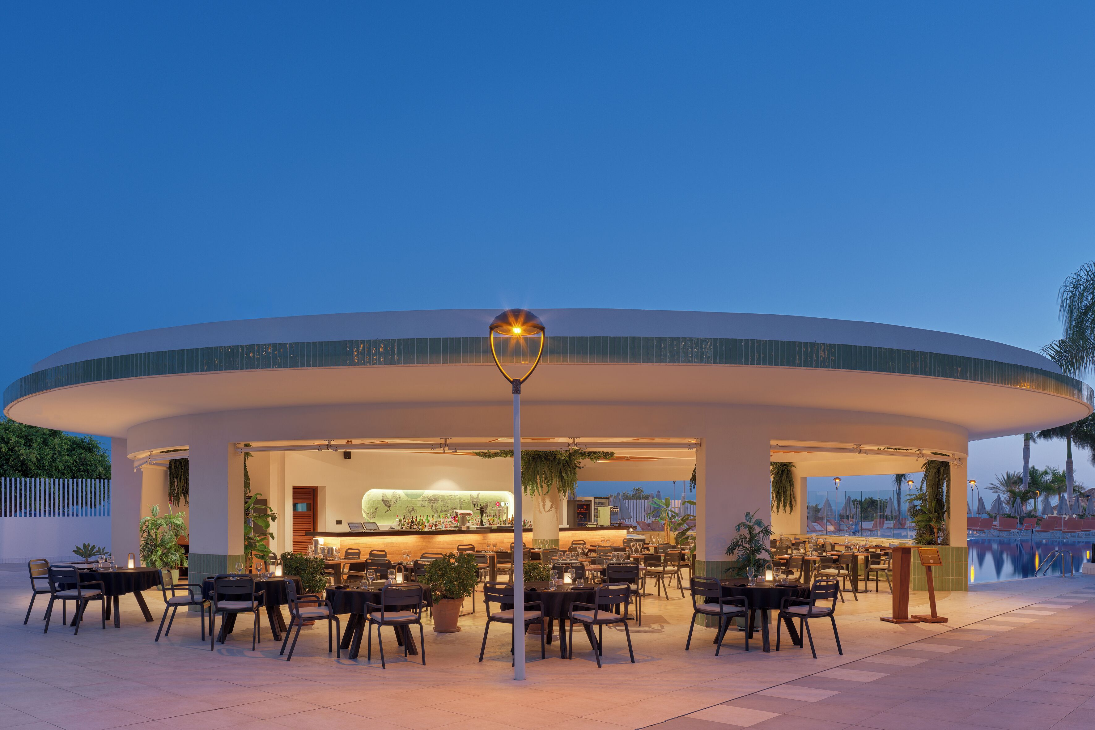 Un espacio de comedor al aire libre con mesas y sillas, un bar y vistas a la piscina.