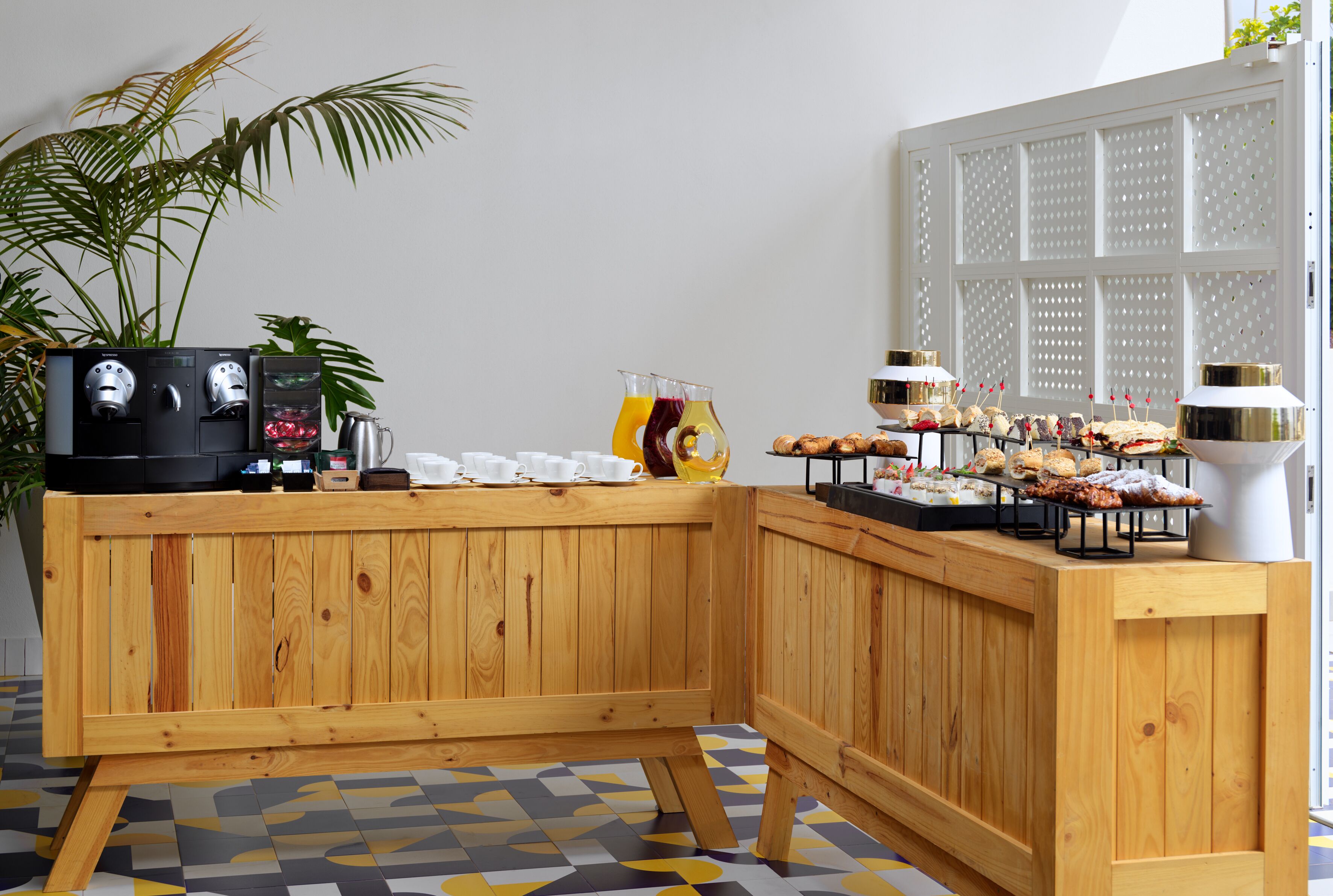 A wooden buffet setup with a coffee machine, juice dispensers, and a variety of pastries and snacks.