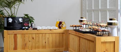 A wooden buffet setup with a coffee machine, juice dispensers, and a variety of pastries and snacks.