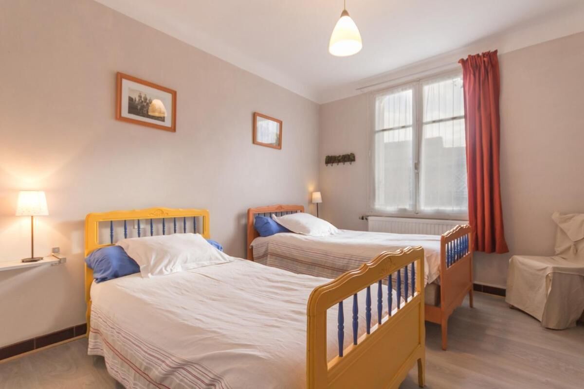 A room with two beds, a window with curtains, a radiator, and a chair.