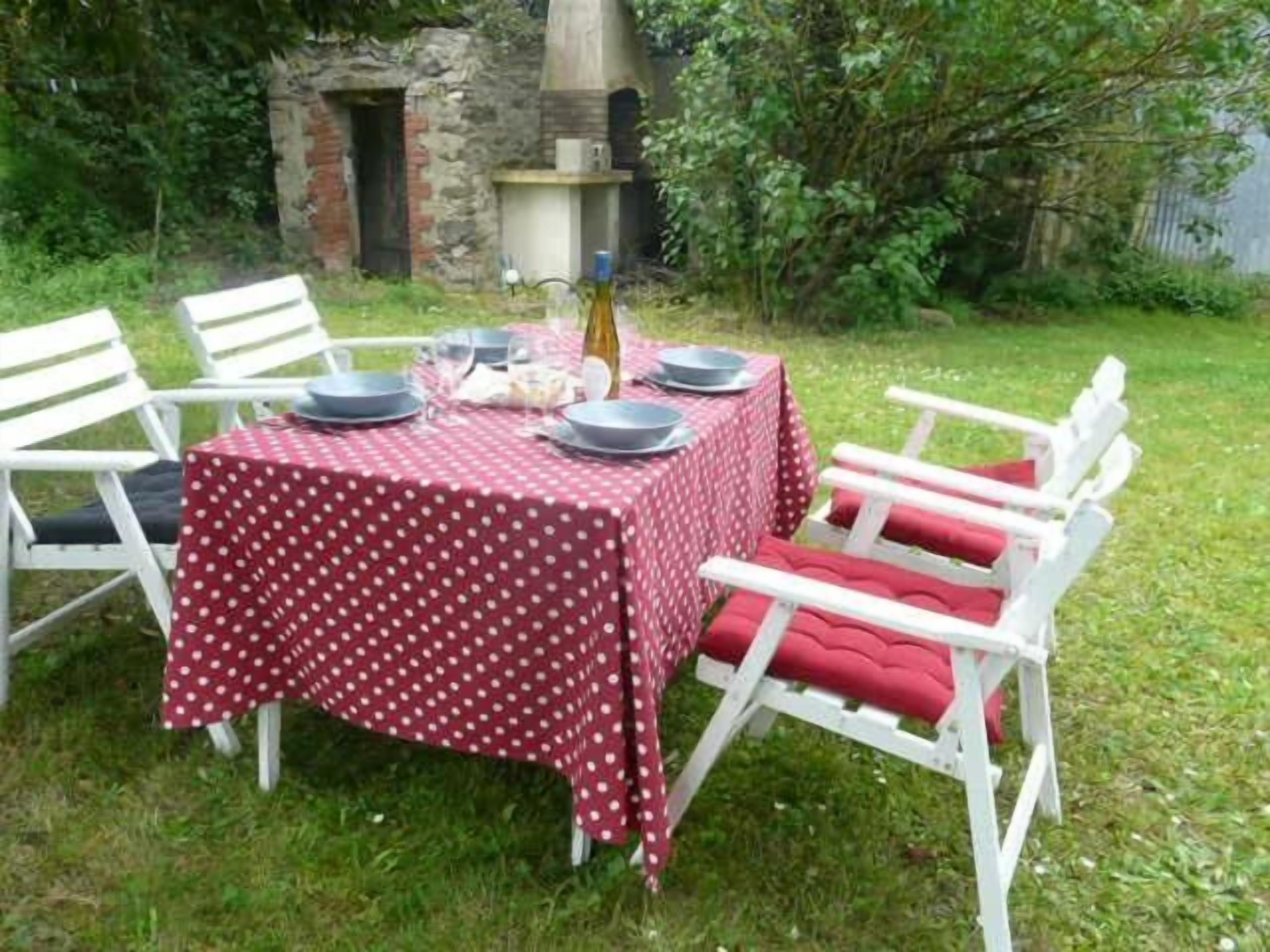 Mesa de comedor al aire libre con mantel de lunares, rodeada de sillas blancas con cojines rojos.