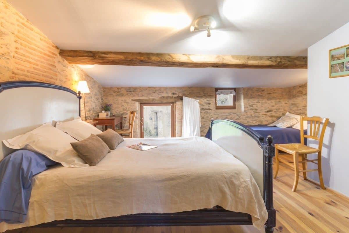 A bedroom with a large bed, a wooden chair, and a stone wall.