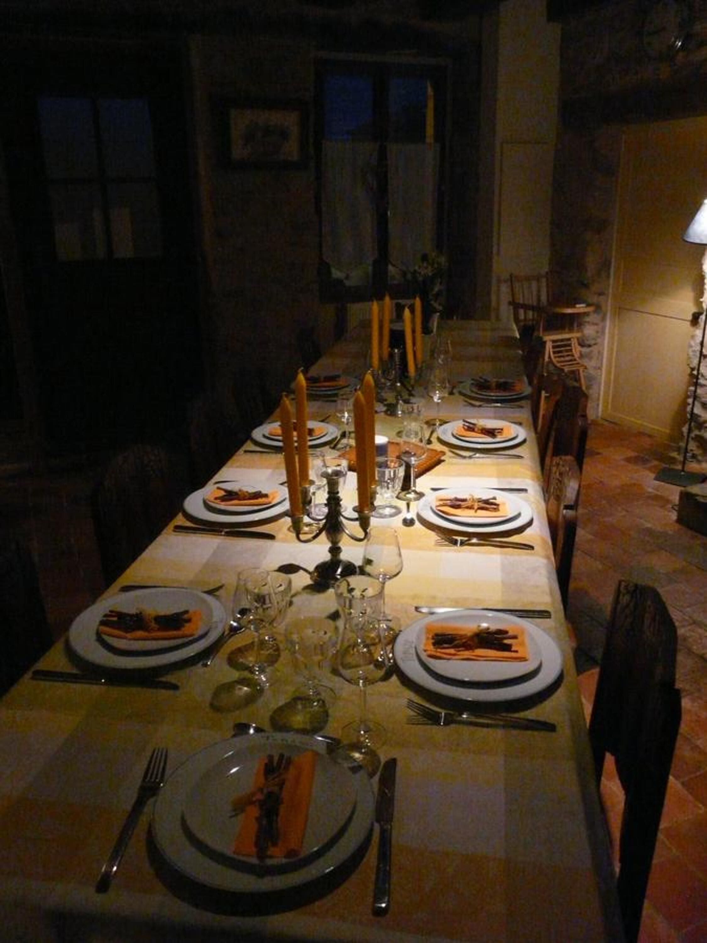 A long dining table set for a meal with candles, plates, cutlery, and glasses.