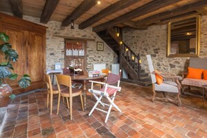 Quarto rústico com parede de pedra, vigas de madeira no teto, mesa de jantar com cadeiras, escada e um espelho grande.
