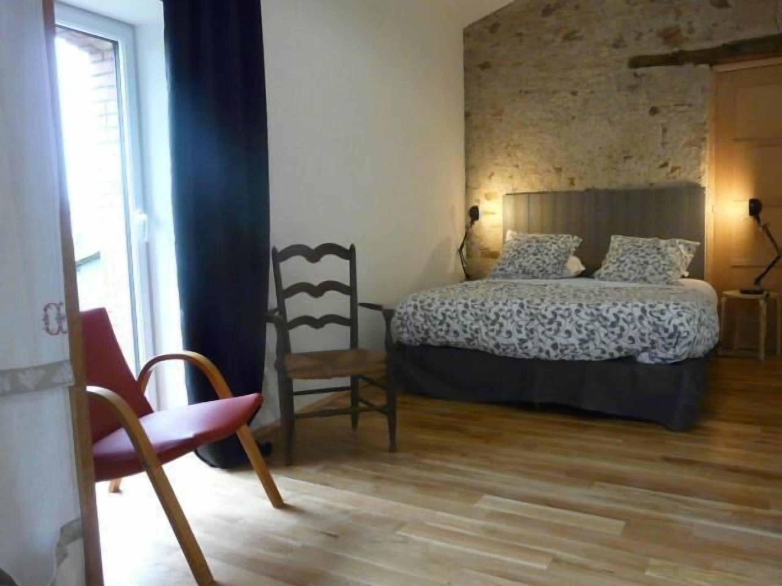 Ein Schlafzimmer mit Bett, Sessel, Lampe und Fenster.