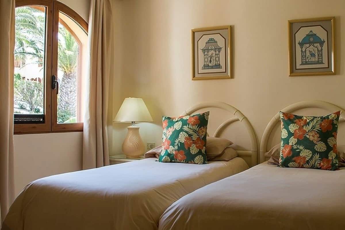 Een tweepersoonskamer met twee bedden, elk voorzien van een bloemenkussen, bedlampjes en ingelijste foto's aan de muur.