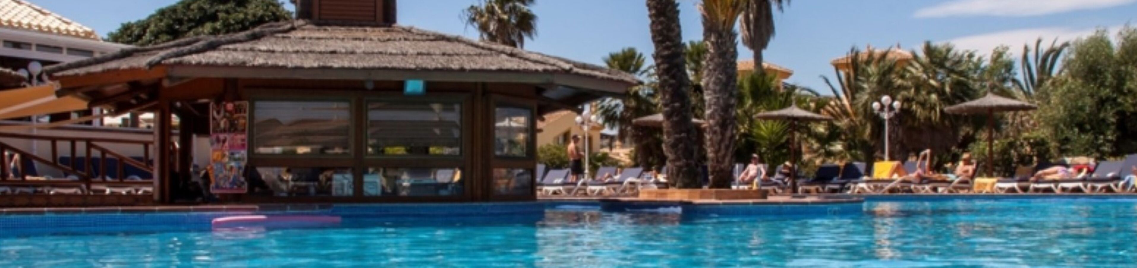 Un área de piscina con sillones de descanso y una estructura de techo de paja.