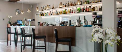 A modern bar area with multiple seating options, a variety of bottles on shelves, and a potted orchid plant.