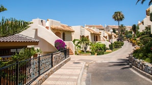Eine Wohnstraße mit Häusern im mediterranen Stil, einem gepflasterten Weg und üppiger Bepflanzung.