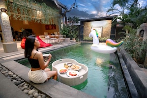 Zona junto a la piscina con una mesa de comedor, un sillón colgante rojo y un juguete flotante.