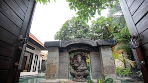 Una entrada arquitectónica tradicional con una estatua de piedra de una deidad, rodeada de abundante vegetación y una piscina.