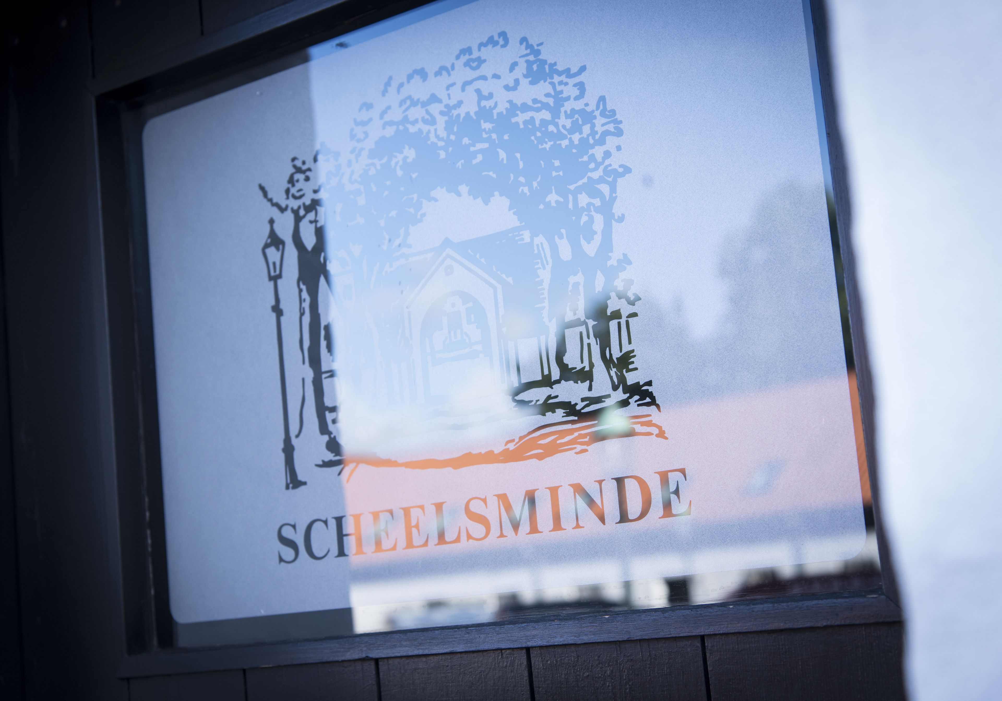 Ein gerahmtes Schild mit dem Schriftzug 'SHEELSMINDER' und einer Darstellung eines Gebäudes mit einem Baum.