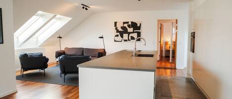 A modern kitchen with a central island, a dining area with a sofa, and a view of the living room.