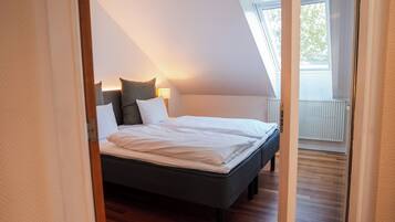 Een slaapkamer met een bed, kussens, een nachtkastje en een raam.