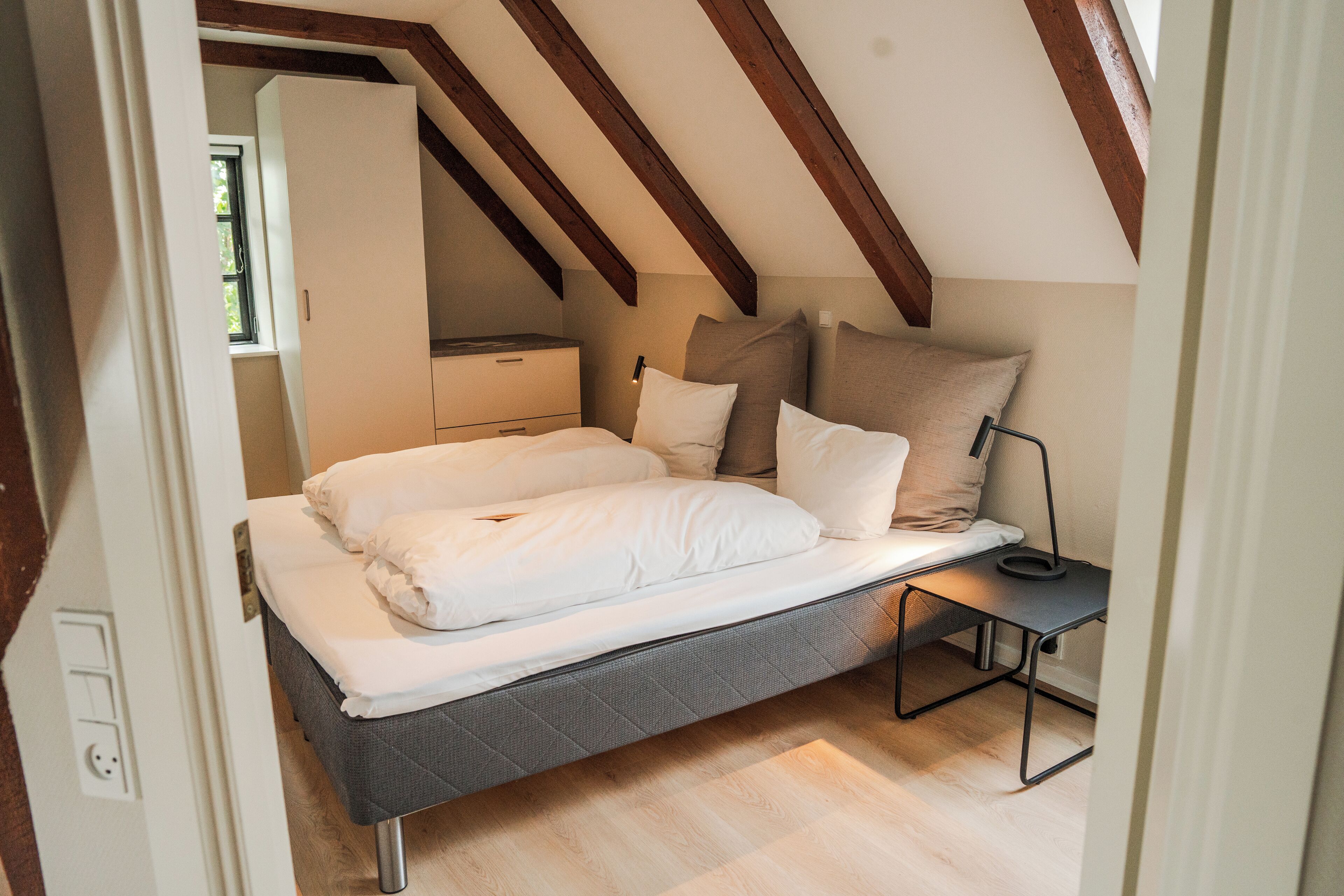 Quarto compacto com cama, mesa de cabeceira e janela.