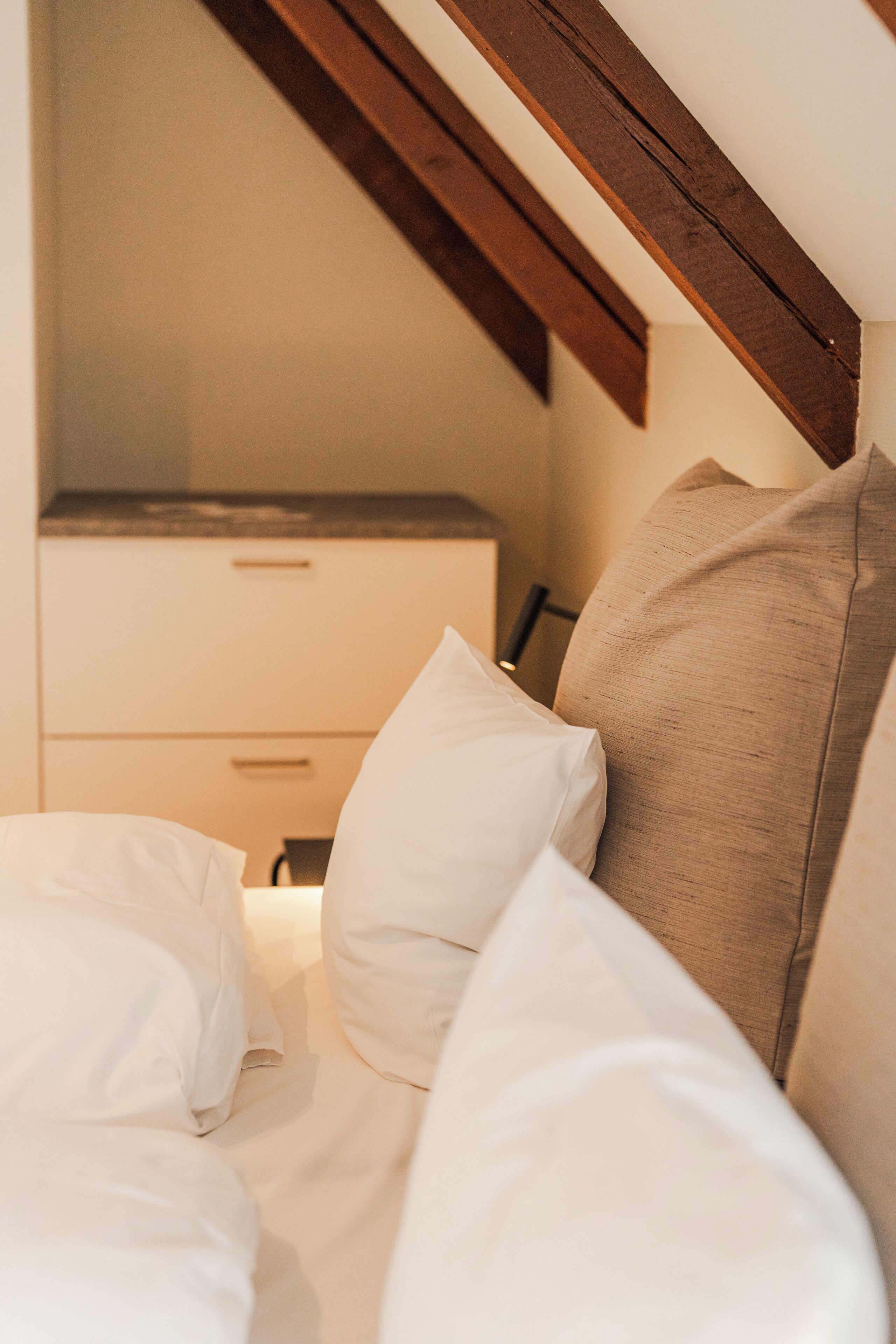 A bedroom with a bed, pillows, a nightstand, and a wooden ceiling beam.