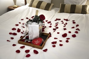 A bed with a champagne bottle, a glass, and a rose in a tray, surrounded by rose petals.